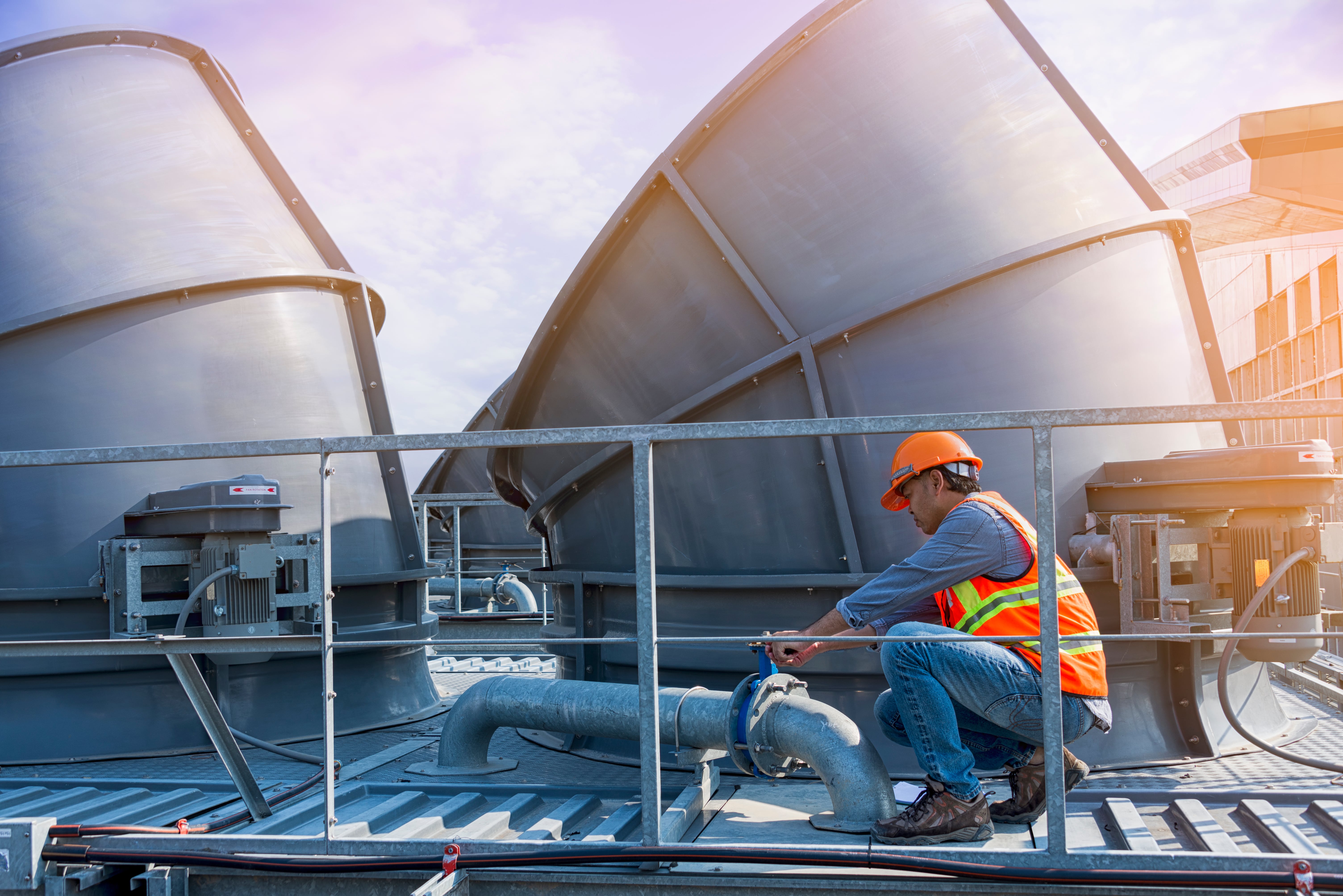 Worker wearing orange helmet fixing the valve of a cooling tower